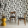 Two wooden chairs with black seats are placed in front of a black and white patterned wall. A yellow side table with vases is to the left of the chairs. Produktbild-Vorschau