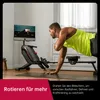 A man is doing a plank exercise in front of a rowing machine with a screen displaying workout instructions. Produktbild-Vorschau