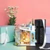 A miniature dollhouse is displayed next to gift-wrapped boxes and a bouquet of flowers, set against a pink and teal background. Anteprima dell’immagine prodotto