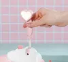 A hand holding a pink heart-shaped shower head with a light on, over a white cloud-shaped bathtub. Produktbild-Vorschau