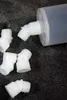 Several white plastic dispensing tips and a larger translucent plastic cylinder are scattered on a dark gray carpeted surface. Produktbild-Vorschau