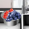 A stainless steel sink strainer filled with blueberries and cherry tomatoes, next to a kitchen faucet. Náhled obrázku produktu