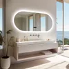 A modern bathroom with a large illuminated mirror, vanity, and a view of the ocean. Podgląd zdjęcia produktu