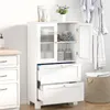 A white wooden bathroom cabinet with glass doors and drawers, containing toiletries and towels, next to a laundry basket. Podgląd zdjęcia produktu