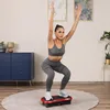 A woman is performing a squat exercise on a vibration plate in a living room. Náhled obrázku produktu