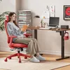A woman is sitting in a red ergonomic office chair and reading a book. She is at a desk with a laptop and other office supplies. The scene is set in a home office environment. Produktbild-Vorschau