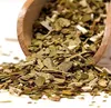 A close-up shot of dried yerba mate leaves and stems spilling out of a wooden scoop. Produktbild-Vorschau