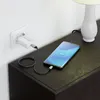 A smartphone is charging on a dark wooden nightstand next to a white lamp. Produktbild-Vorschau