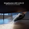 A hand-held vacuum cleaner is shown being used to clean under a dark table, with the built-in LED light illuminating the area. Produktbild-Vorschau