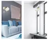 A split image showing two different interior settings with a wall lamp. The left side shows a living room with a sofa and the lamp on a gray wall. The right side shows a room with a white brick wall and a window, with the lamp mounted on a pillar. Produktbild-Vorschau