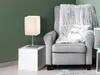 A cozy corner with a gray armchair, a fluffy blanket, a pillow with text, and a white table with a lamp. Produktbild-Vorschau