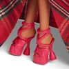 Close-up of a doll's feet wearing pink platform heels, with a red plaid fabric in the background. Náhľad obrázku produktu