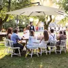 A group of people are gathered around a table outdoors, enjoying a meal under a large umbrella. Náhled obrázku produktu