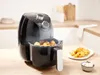 A black air fryer on a wooden countertop, with cooked potatoes on a plate next to it. Produktbild-Vorschau