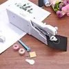 A white handheld sewing machine is shown on a wooden surface with various sewing accessories. Náhled obrázku produktu