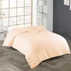 A bed with a peach-colored duvet and pillow in a room with a large window and a bedside table. Produktbild-Vorschau