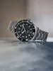 A silver watch with a black face is displayed on a reflective surface. Náhled obrázku produktu