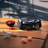 A black waffle maker is placed on a wooden table, with a bowl of raspberries, two eggs, and some kitchen utensils nearby. Produktbild-Vorschau