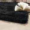 A close-up shot of a black shaggy rug with an open book on it, placed on a light wooden floor. Produktbild-Vorschau