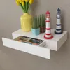 A white floating shelf with a drawer pulled out, displaying books and decorative items like lighthouses and plants. Náhľad obrázku produktu