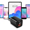 A black USB charger with a digital display is shown in the foreground, with several smartphones and a tablet in the background. Produktbild-Vorschau