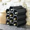 A black hexagonal wine rack holding several bottles of wine, placed on a countertop in front of a stone wall. Produktbild-Vorschau