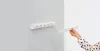 A white retractable clothesline mounted on a light gray wall, with a hand extending a part of it. Náhled obrázku produktu