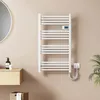 A white electric towel warmer is mounted on a light beige wall in a bathroom setting. Náhľad obrázku produktu