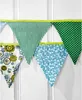 A string of fabric bunting flags with different patterns, hanging against a white wooden background. Produktbild-Vorschau