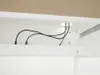 A close-up view of cables passing through a hole in a white cabinet or desk. Produktbild-Vorschau
