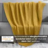 A yellow knitted blanket draped over a sofa. Náhľad obrázku produktu