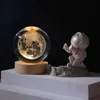 A crystal ball with a 3D moon inside, lit from within, sits on a wooden base next to a small astronaut figurine on a lunar surface. Náhled obrázku produktu