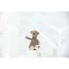 A small, brown teddy bear sits on a white bucket in a whimsical, snowy forest scene made of white paper cutouts. Podgląd zdjęcia produktu