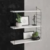 A white three-tiered shelf unit with decorative items on a wall split between black and gray concrete textures. Anteprima dell’immagine prodotto