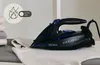 A black and blue Zeegma iron is placed on an ironing board next to a stack of folded clothes. A circular graphic with a flame crossed out and the text 'AUTO OFF' is visible in the upper left corner. Produktbild-Vorschau