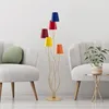 A colorful floor lamp is placed between two chairs in a living room setting. Produktbild-Vorschau