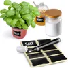 A collection of items for labeling and storing kitchen ingredients, including a basil plant, jars of honey and salt, and a sheet of chalkboard labels with a marker. Produktbild-Vorschau