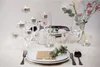 A table setting with multiple tea lights in glass holders, flowers, and place settings. Podgląd zdjęcia produktu