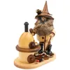 Ein Erzwichtel mit spitzem Hut und buschigem Bart steht neben einem kleinen Erzofen aus Holz und hält Werkzeuge in den Händen während um ihn herum kleine Details wie ein Pilz und Holzstücke zu sehen sind Produktbild-Vorschau