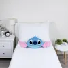 A blue Stitch plush pillow is placed on a white bed in front of a white pillow. Voir les images du produit