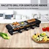 A raclette grill set is displayed on a wooden table, with food and ingredients arranged around it. Produktbild-Vorschau