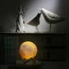 A moon lamp is displayed on a wooden stand, with decorative bird figurines and an angel statue in the background. Produktbild-Vorschau