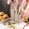 A person is arranging kitchen utensils in a holder next to a cutting board with vegetables and bread. Produktbild-Vorschau
