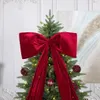A large red velvet bow is placed on top of a decorated Christmas tree. Náhľad obrázku produktu