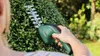 A person is using a cordless hedge trimmer to trim a bush in a garden. Anteprima dell’immagine prodotto