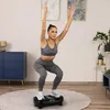 A woman is performing a squat exercise on a vibration plate in a living room. Náhľad obrázku produktu