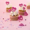 Several cupcakes decorated with pink heart-shaped toppers and sprinkles on a pink background. Produktbild-Vorschau