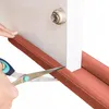 A close-up shot of someone cutting a brown foam door seal with scissors. Náhled obrázku produktu