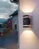 An outdoor wall light illuminates a deck and house exterior at dusk. Produktbild-Vorschau