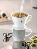 A coffee dripper with a mug and coffee grounds is being prepared with hot water being poured in. Produktbild-Vorschau